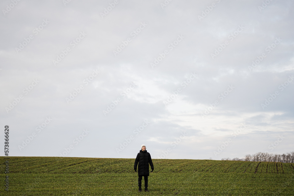 Teen boy wearing black jacket and white hat outside, enjoys in the early spring field.. Teen boy wearing black jacket and white hat outside, enjoys in the early spring field..