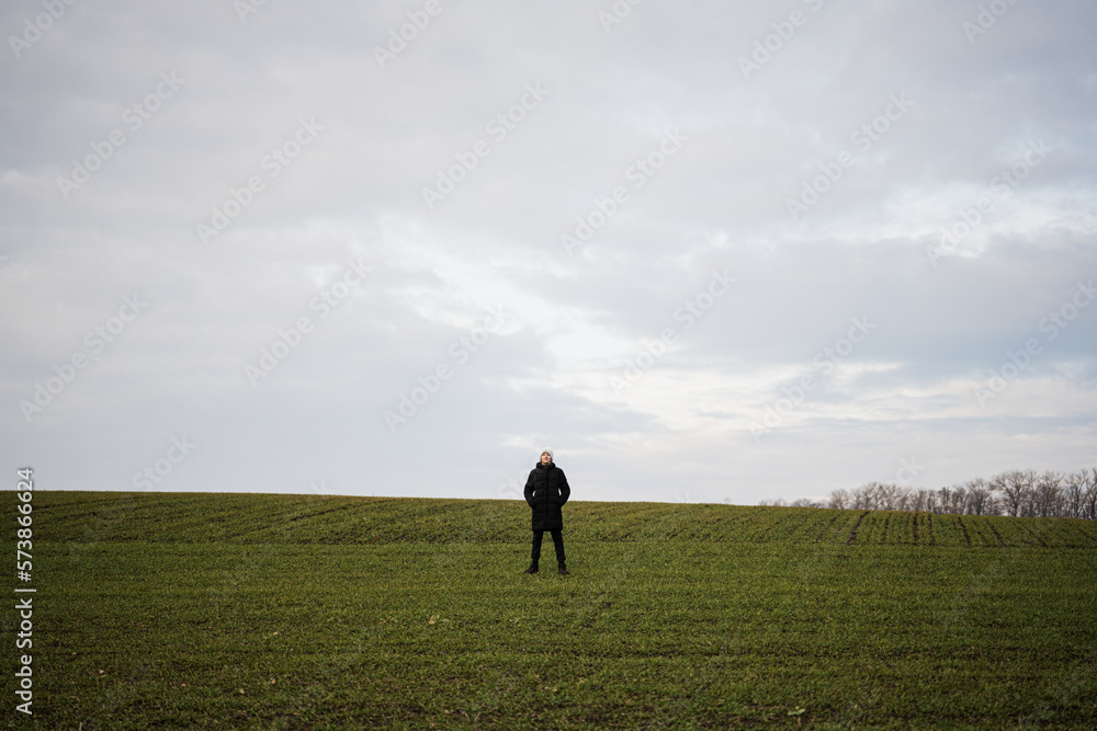 Fototapeta premium Teen boy wearing black jacket and white hat outside, enjoys in the early spring field..