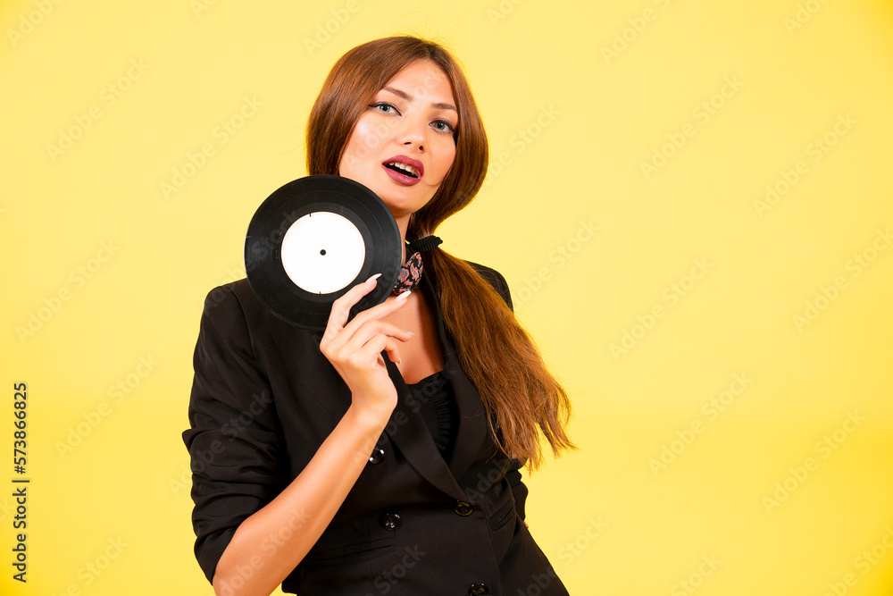 Fototapeta premium girl in a black suit on a yellow background with a record in her hands, music, the girl shows emotions