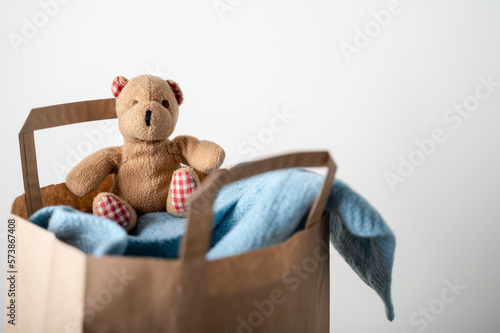 Paper bag with used clothing and bear toy to donate on wooden table. Reuse © molenira