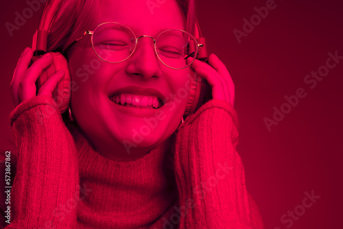 Portrait of a happy girl listening music on headphones isolated on magenta background. Monochromatic picture, viva magenta, color of the year. photo