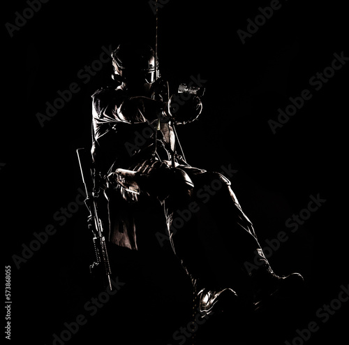 Silhouette of police officer in tactical gear descending from a height, rope exercises with weapons. Tactical rappelling, anti-terror or counter terrorism operation in darkness in rappelling harness