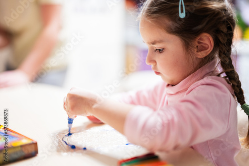 Little girl with pigtails decorating art with glitter decor tube of paint.