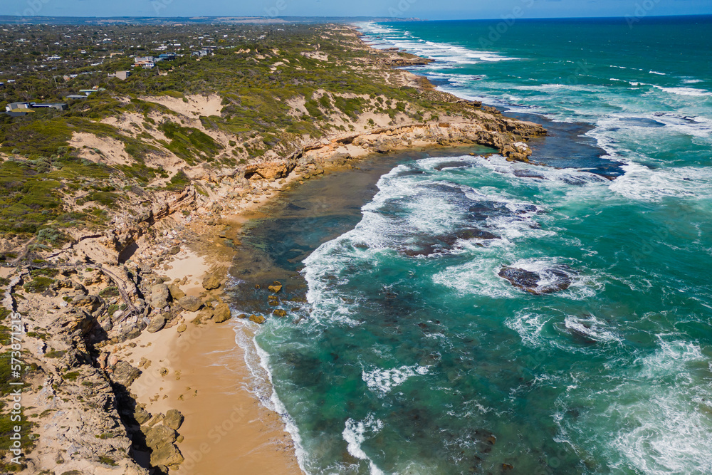 An aerial view as Waves crash over sand and rocks on a sunny day in Bridgewater Bay in Blairgowrie, Victoria, Australia
