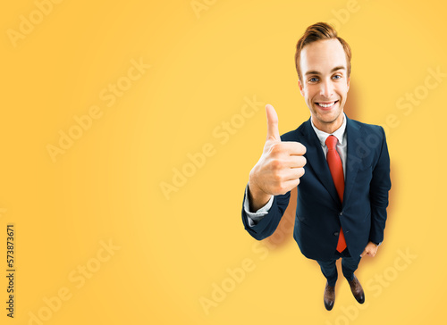 Full body businessman in black suit showing thumb up like, agree hand sign gesture on yellow background. Comic look happy man. Cartoon style character with big head. Funny face. Copy space mockup area