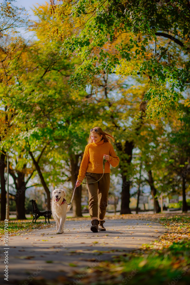Belgrade, Serbia. November 10th, 2022. Cheerful young woman walking her golden retriever in a park on a sunny day.