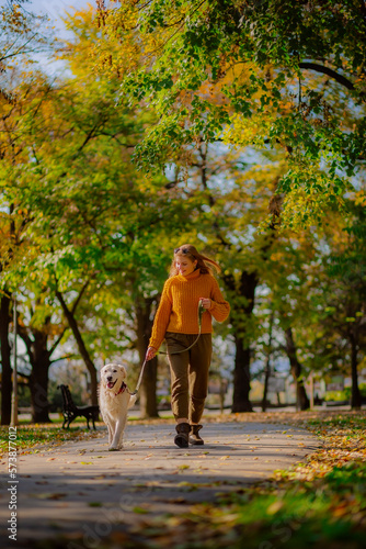 Belgrade, Serbia. November 10th, 2022. Cheerful young woman walking her golden retriever in a park on a sunny day.