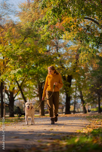 Belgrade, Serbia. November 10th, 2022. Cheerful young woman walking her golden retriever in a park on a sunny day.