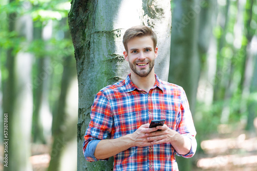 photo of happy man messaging on phone in the forest. man messaging on phone outdoor.