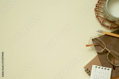 Obraz na płótnie Brown notebook, calendar, eyeglasses, cup of milk, pencil on yellow desk background. flat lay, top view, copy space w salonie