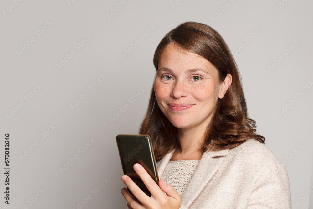Friendly smiling woman using smartphone texting messaging friend checking social media feed browsing internet hold mobile phone against grey studio wall banner background Friendly smiling woman using smartphone texting messaging friend checking social media feed browsing internet hold mobile phone against grey studio wall banner background