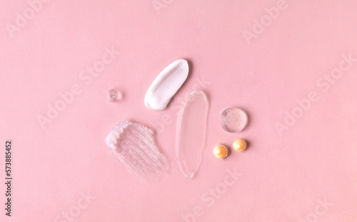 Swatches from various cosmetic products, drops of lotion, smears of creams, gels and scrubs on pink background