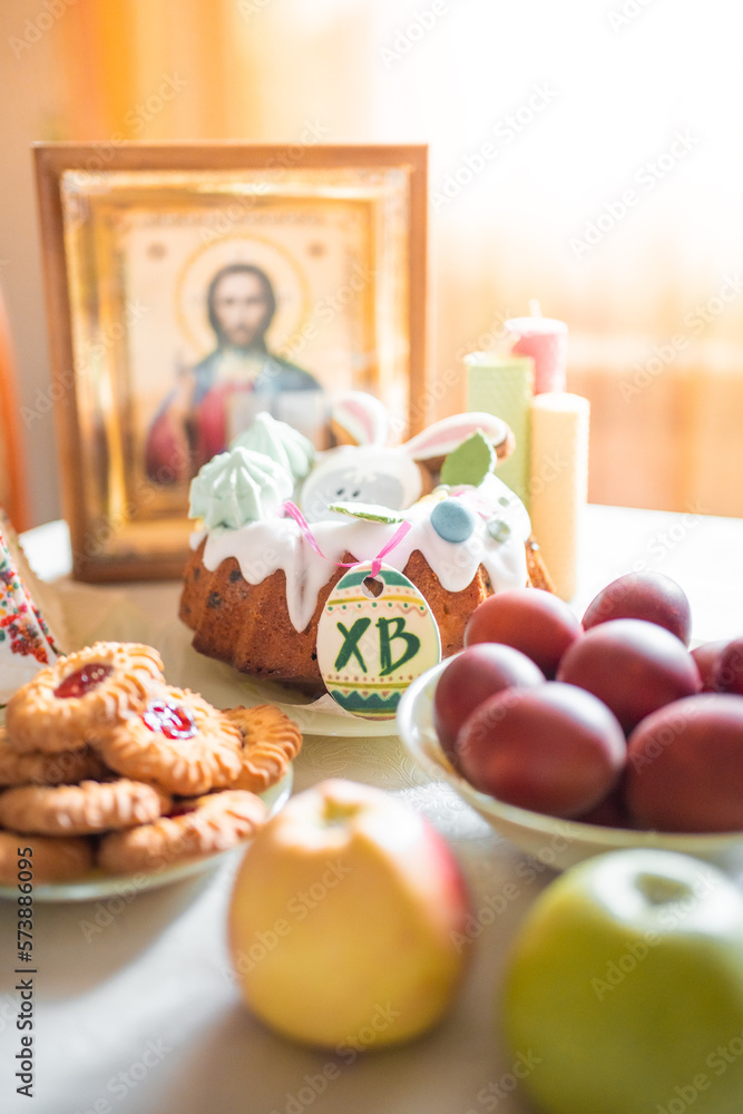 Easter cake with painted eggs, apples and cookies on table in home kitchen. Church icons and candle on background. Orthodox religion theme. Easter cake with painted eggs, apples and cookies on table in home kitchen. Church icons and candle on background. Orthodox religion theme.