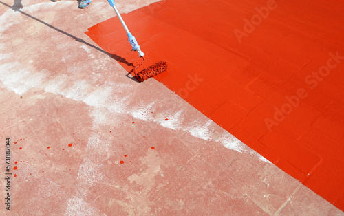 Waterproofing the roof of the building with red rubber waterproofing paint spread with a roller
