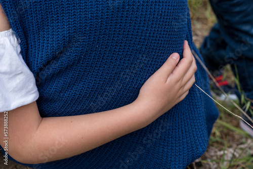 Child's hand hugging a parent in a blue sweater.