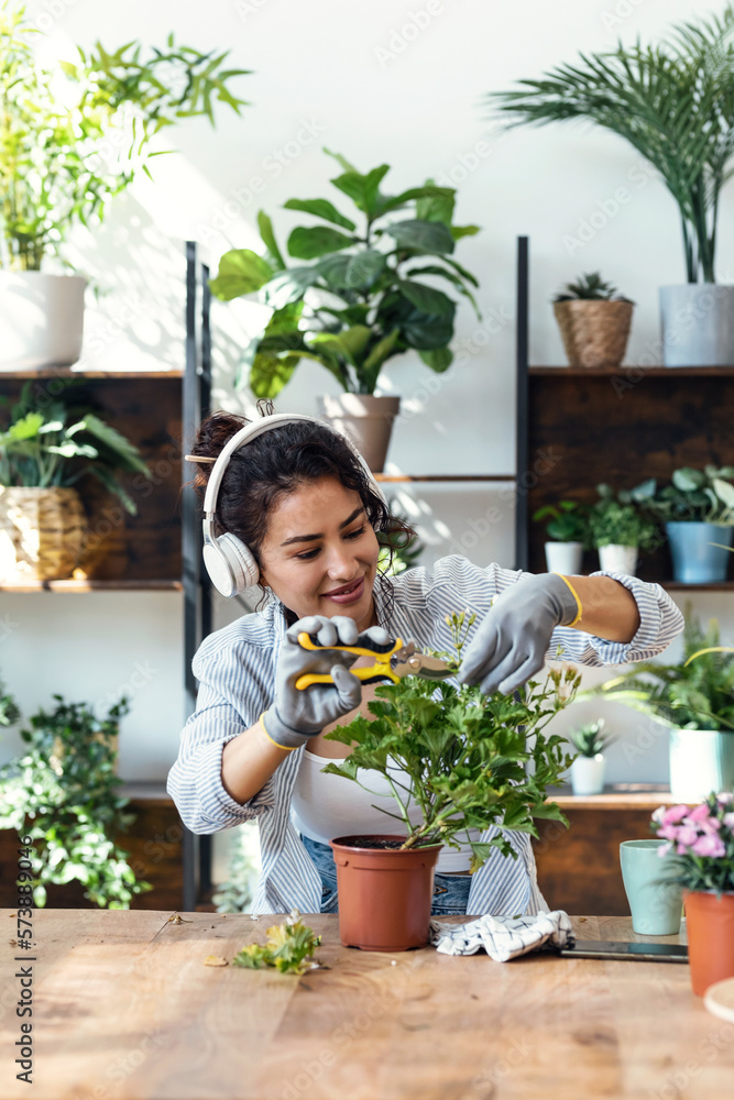 Beautiful smiling woman arranging plants and flowers while listening music in a greenhouse Beautiful smiling woman arranging plants and flowers while listening music in a greenhouse