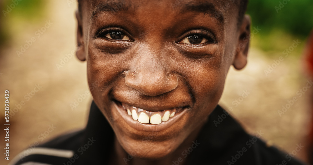 Close Up Portrait of a Playful Authentic African Kid Looking at the Camera and Smiling Intensely with a Blurry Background. Happy Energetic Black Boy Sharing his Beautiful Big Smile with the World Close Up Portrait of a Playful Authentic African Kid Looking at the Camera and Smiling Intensely with a Blurry Background. Happy Energetic Black Boy Sharing his Beautiful Big Smile with the World