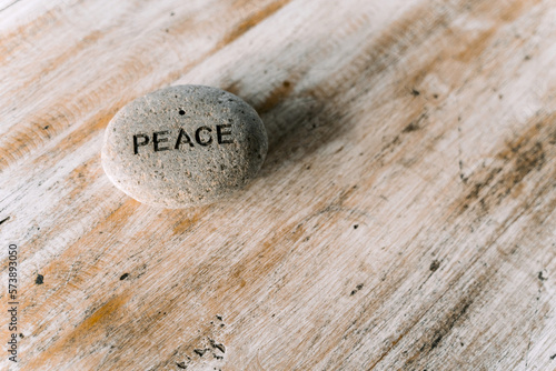 A grey stone with the inscription peace lying on a wooden table.