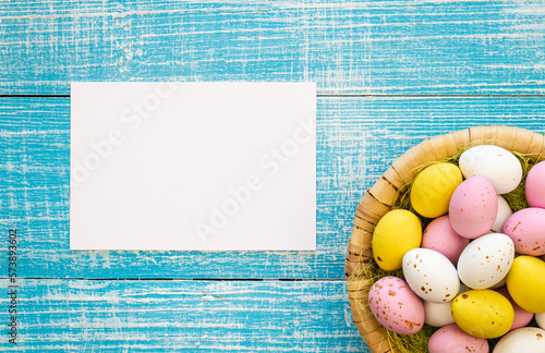 Easter background with colorful chocolate eggs and a blank piece of paper, on a blue wooden background, flat lay, Easter holiday concept, copy space.