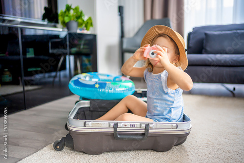 Little girl with suitcase baggage luggage and inflatable life buoy playing with toy camera and ready to go for traveling on vacation