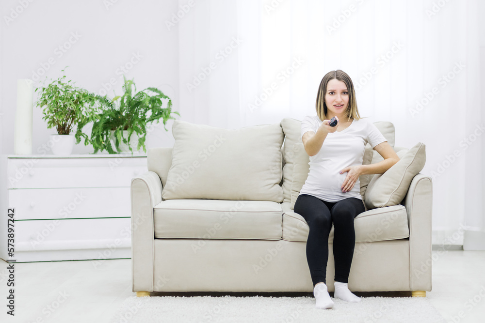Photo of pregnant young woman with remote control in hand. Photo of pregnant young woman with remote control in hand.