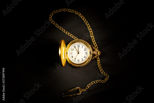 Golden pocket watch on satin background showing five minutes to midnight