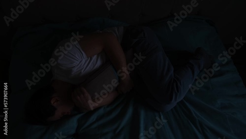 Depressed suicidal man in darkness anxiety hugging pillow on couch pulsing light his breast. Sad desperate person with chronic disease difficulties ask for help with his hand reaching camera