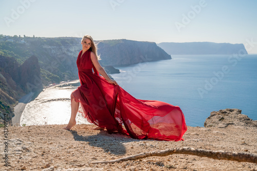 A woman in a red flying dress fluttering in the wind  against the backdrop of the sea.