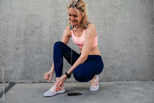 Sporty girl tying shoelaces near the wall in headphones