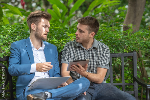 Two businessman or gay sitting at chair in park while using digital tablet and paper work plan for talk discussion team working online togetherness while consulting. © BESTIMAGE
