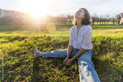 Young caucasian pretty woman in a white shirt sitting on the green grass enjoying the spring sun in the countryside