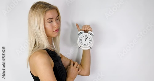 An attractive blonde haired woman holding up an old style alarm clock that is set to 1 o'clock, waking up at 1am or 1pm concept, filmed in 4k footage photo