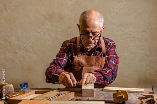 Old carpenter working in his workshop, using hand tools to shape a piece of wood