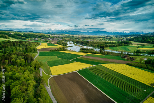 Blick über den Flachsee (Reuss). Ein buntes Mosaik. an Rapsfeldern, Ackerflächen und grünen Wiesen ziehen sich hin zu den Voralpen und Bergen am Horizont.