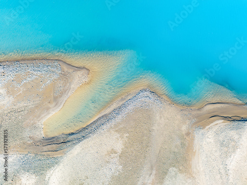 Clear azure water in a mountain lake. The shore with stones. View of the water from a drone. Landscape from the air. Natural landscape as wallpaper.