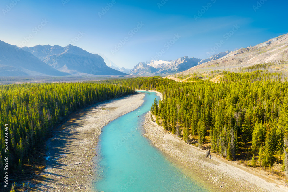 A drone view of the river in the mountains valley. An aerial view of an autumn forest. Winding river among the trees. Turquoise mountain water. Landscape with soft light before sunset.