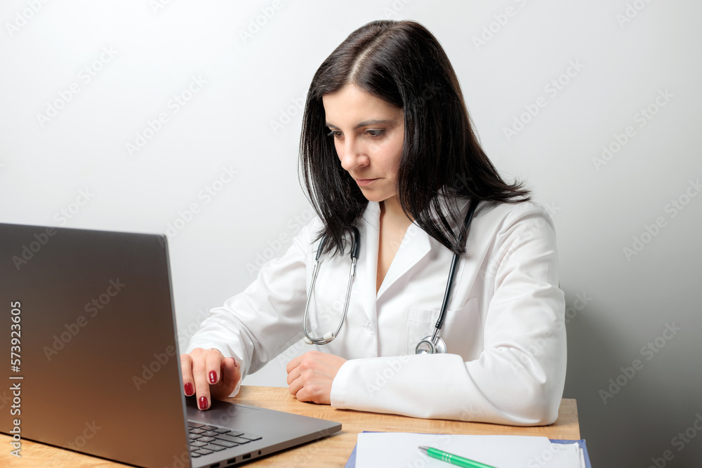 Female doctor, medic physician in white coat with stethoscope working on laptop at table Female doctor, medic physician in white coat with stethoscope working on laptop at table