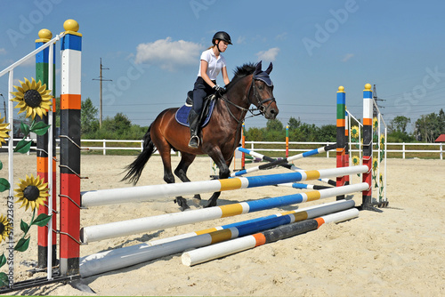 Girl riding a horse jumps over a barrier on training. © Mykola