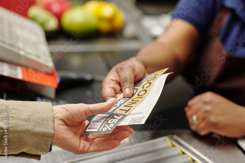 Hand of young African American female cashier passing discount coupon and receit to customer over checkout counter in supermarket photo