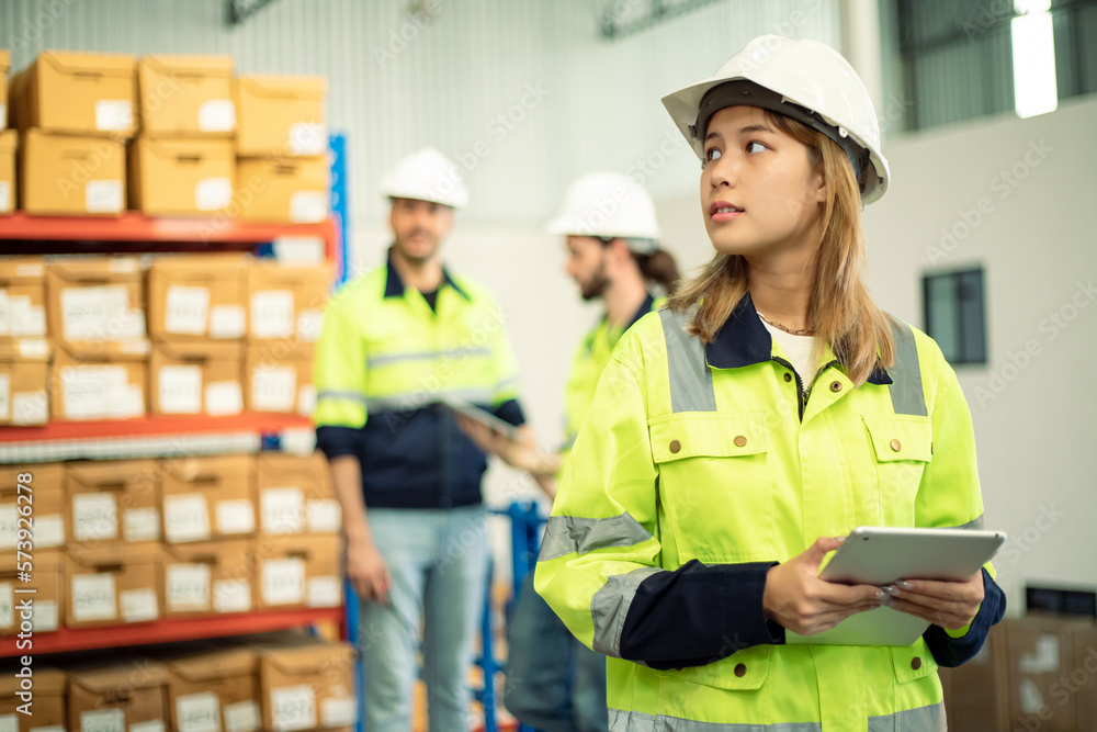 Professional female worker with teamwork wearing hard hat uses digital tablet computer for work. Goods and supplies on shelves with goods background in warehouse.logistic and business export Professional female worker with teamwork wearing hard hat uses digital tablet computer for work. Goods and supplies on shelves with goods background in warehouse.logistic and business export