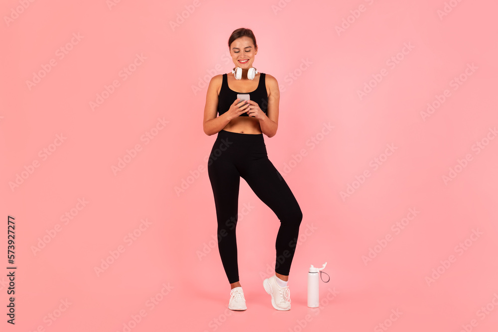 Happy Fit Lady In Sportswear Using Smartphone While Standing Over Pink Background, Happy Fit Lady In Sportswear Using Smartphone While Standing Over Pink Background,