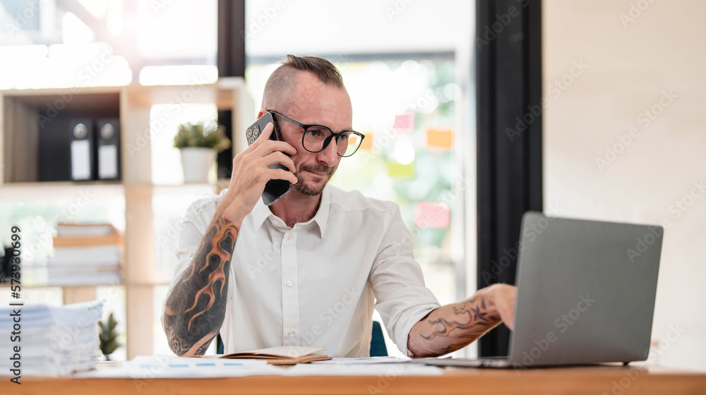 Handsome mature businessman is talking on the mobile phone and smiling while working in office Handsome mature businessman is talking on the mobile phone and smiling while working in office