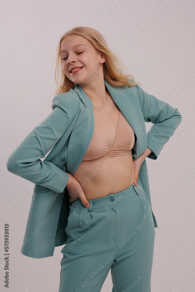 Young blond teenage girl in light green business suit smiling. Lady in beige top and jacket pose in white background. Girl portrait. Young blond teenage girl in light green business suit smiling. Lady in beige top and jacket pose in white background. Girl portrait.