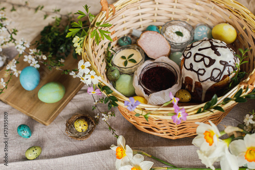 Traditional Easter food in basket. Homemade easter bread, natural dyed easter eggs, ham, beets, butter, cheese on rustic table with spring blossoms and linen napkin. Top view