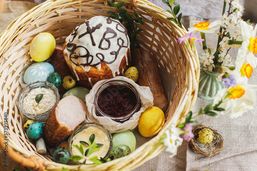 Traditional Easter food in basket. Homemade easter bread  natural dyed easter eggs  ham  beets  butter  cheese on rustic table with spring blossoms and linen napkin. Top view