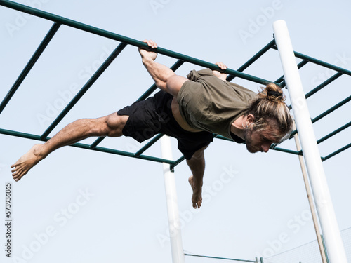 Young caucasian man doing calisthenics exercise hanging on the bars