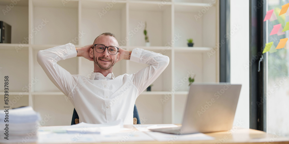Satisfied with work done. Happy young man working on laptop while sitting at his working place in office Satisfied with work done. Happy young man working on laptop while sitting at his working place in office