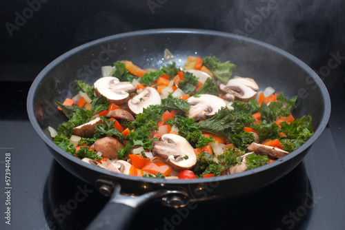 Kale, mushrooms, onions and red peppers frying in a pan on a convection oven