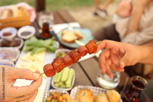 a person is holding a skewer of sausage on a stick with other people around it and a picnic table with food © erdin