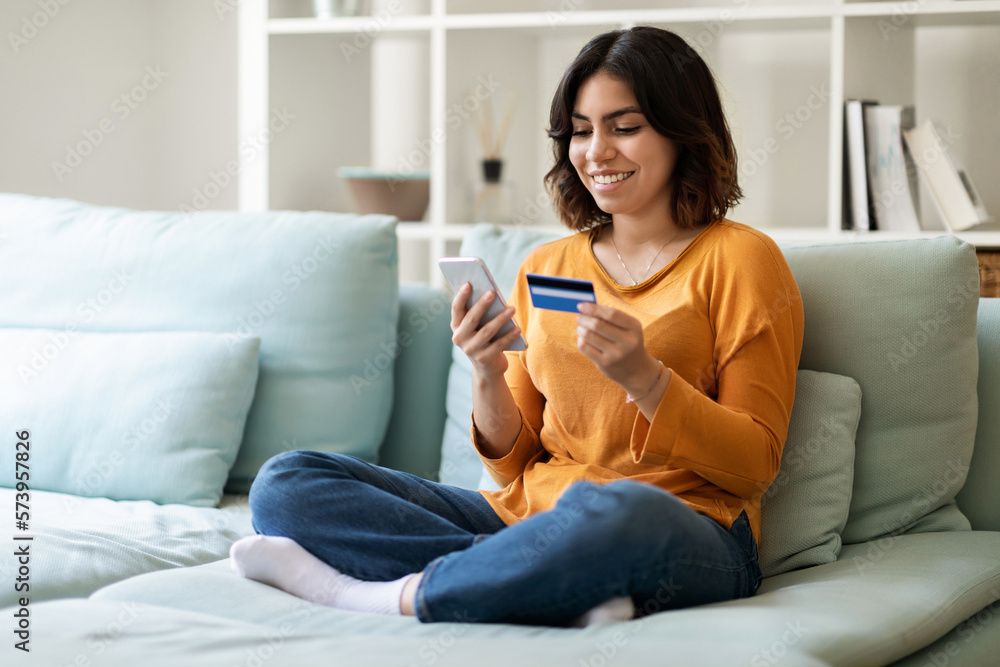 Mobile Payments. Young Arab Female Using Smartphone And Credit Card At Home Mobile Payments. Young Arab Female Using Smartphone And Credit Card At Home